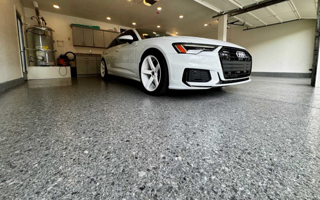 Premium polyurea garage floor coating with gray flake finish and ceramic sealer installed in a residential garage in Las Vegas with a white sedan parked inside